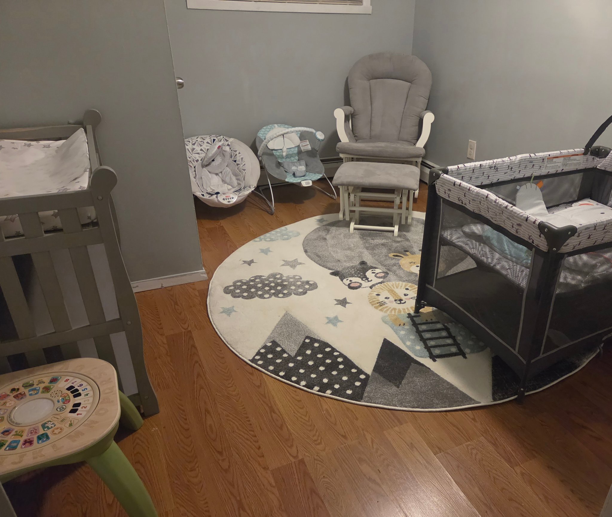 Cozy infant room with crib, pack-n-play, glider and animal rug at Taylor's Bright Beginners